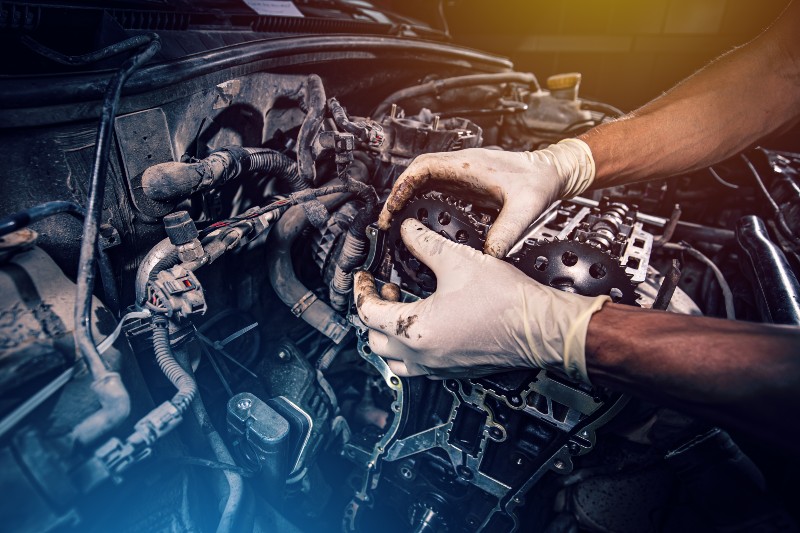 Mechanik w rękawiczkach naprawia silnik samochodowy, montując zębatki rozrządu.