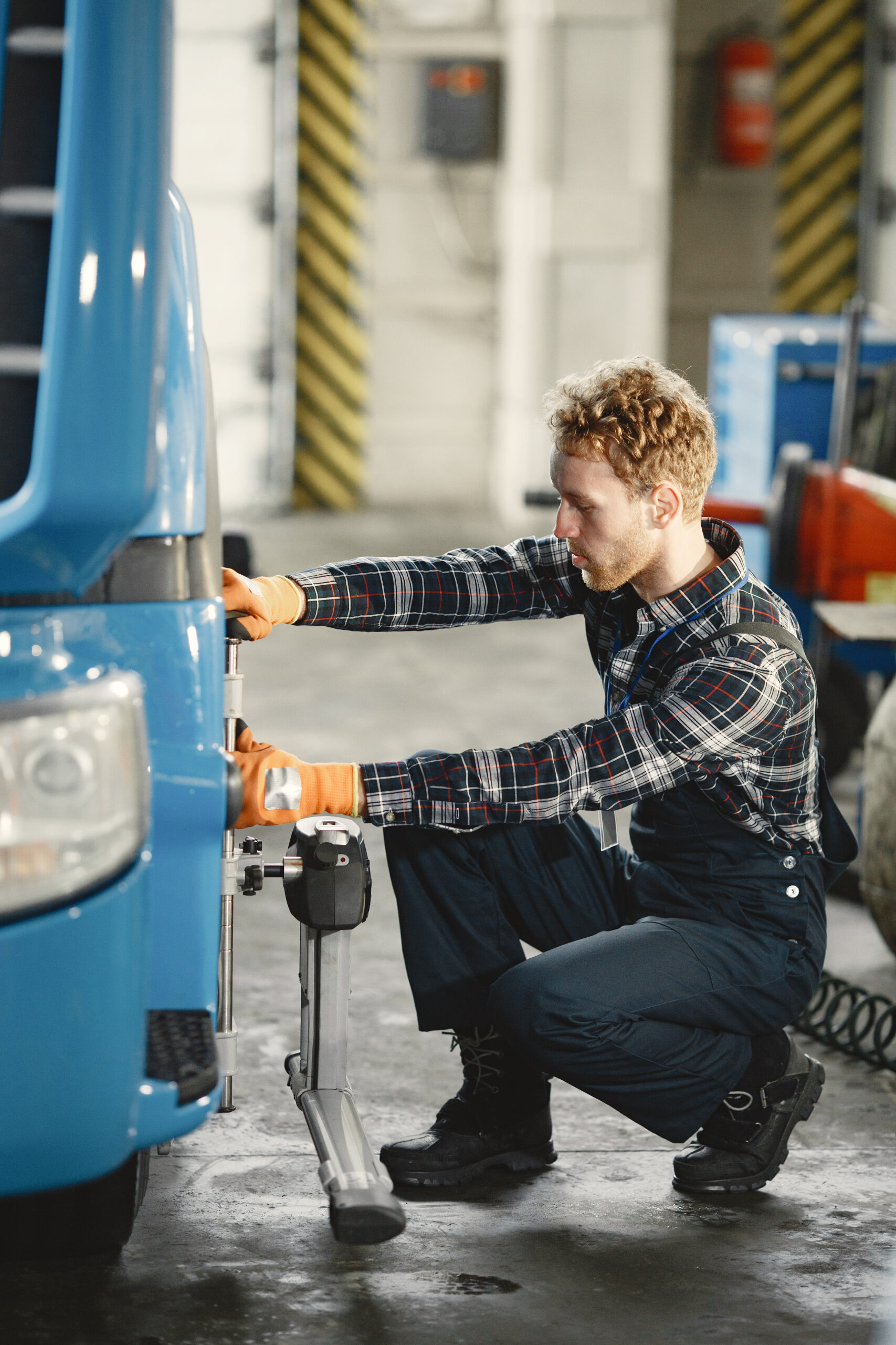 Mechanik w kombinezonie i rękawicach naprawia niebieski samochód ciężarowy w garażu.